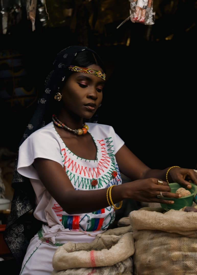 A market trader in an embroidered dress serving from sacks at her stall